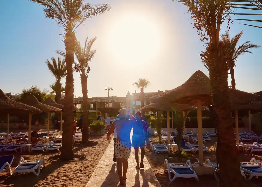 Guests walking between palm trees and sun loungers towards the sea at a Sharm El Sheikh hotel.